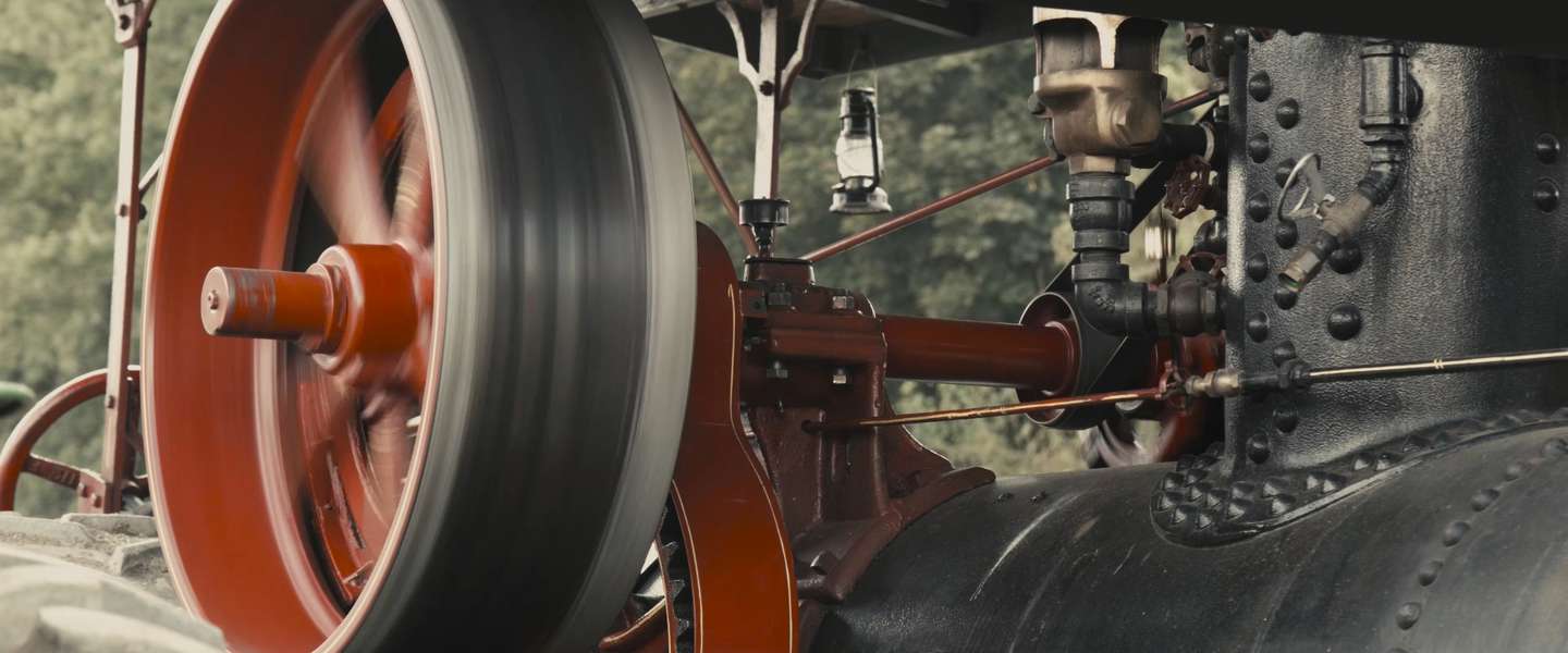 A close up of some of the bright red moving parts of an antique steam engine rigged to power a sawmill.